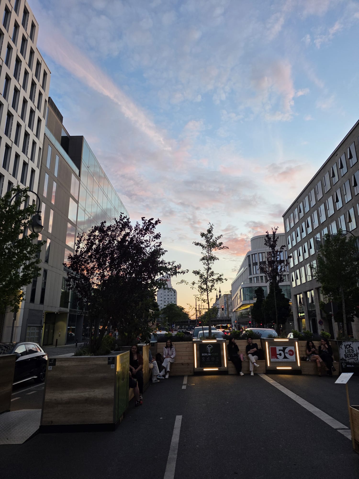 Menschen sitzen am Abend auf den Bänken der Berlin-Cube-Anlage in der Kantstraße in Berlin